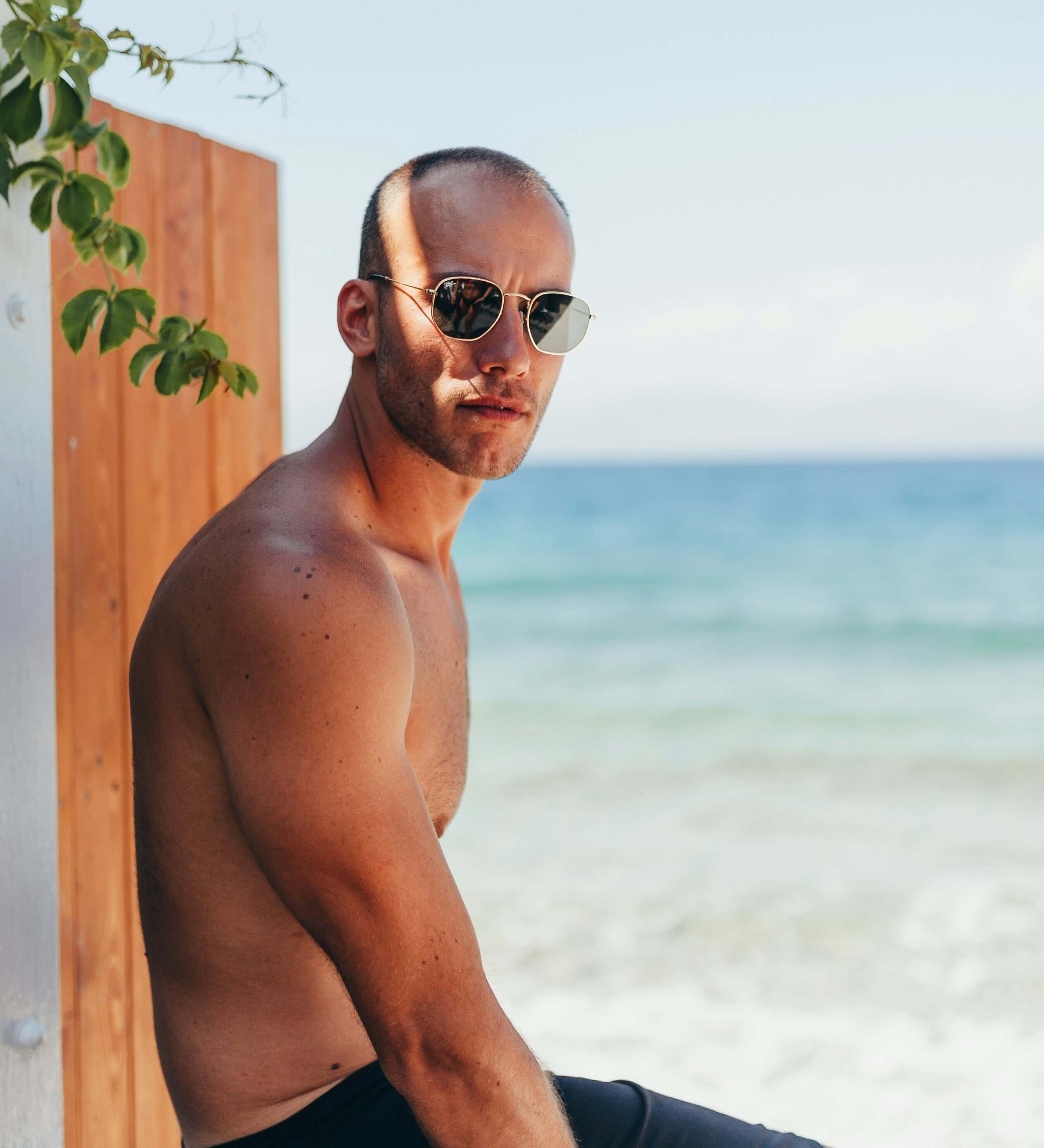 A man in sunglasses sits casually on a stone wall, enjoying the outdoors at the beach.